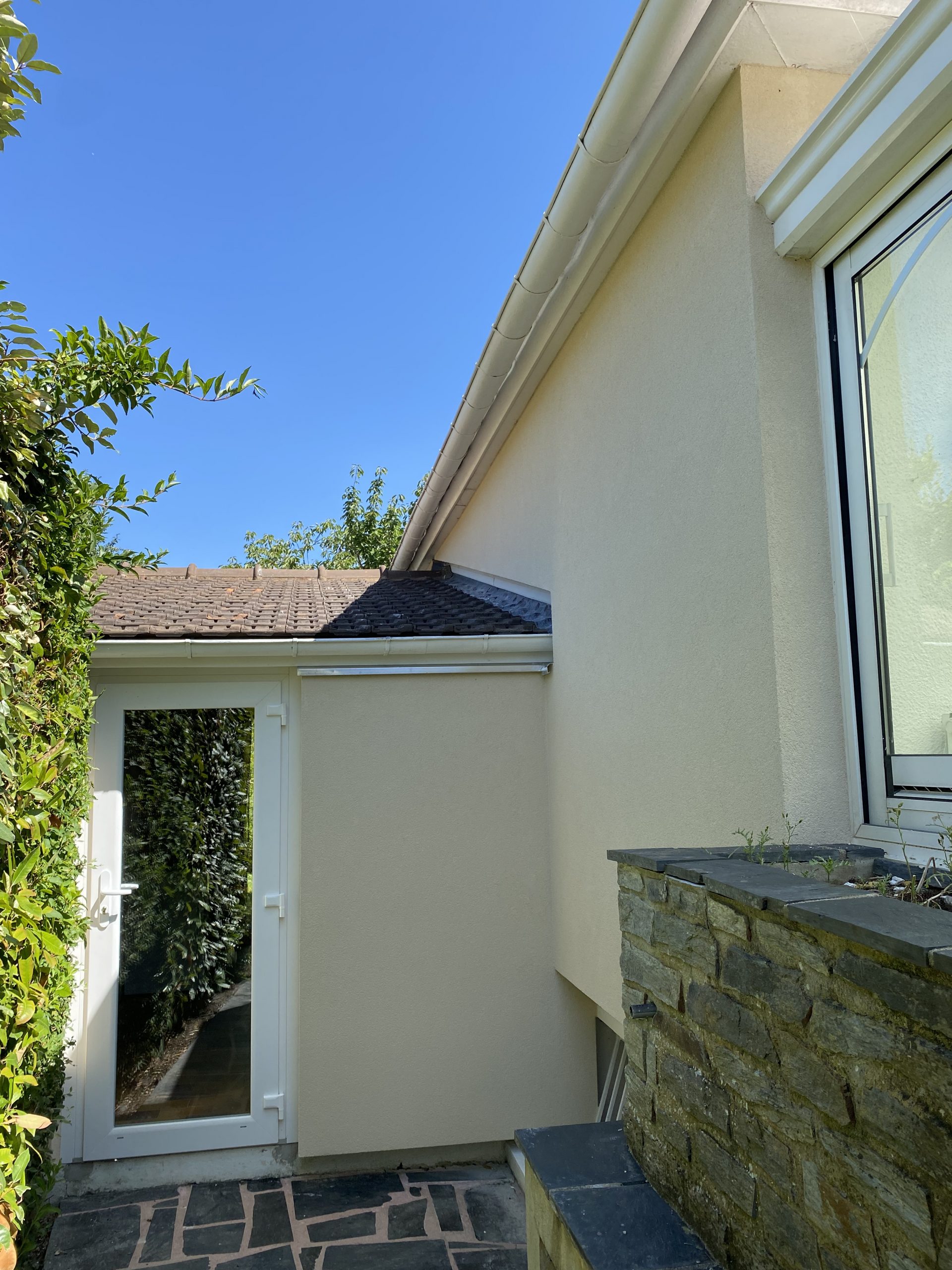 Façade jaune claire avec arbuste à gauche, terrasse et porte blanche. C'est une photo prise par IDE Habitat.
