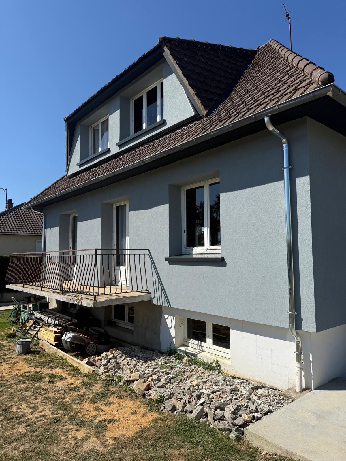 Maison avec façade bleue claire, escalier et jardin. Le ciel est bleu. La photo a été prise par IDE Habitat.